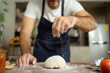 Happy cheerful Italian chef making a fresh pizza dough on wooden table in kitchen.