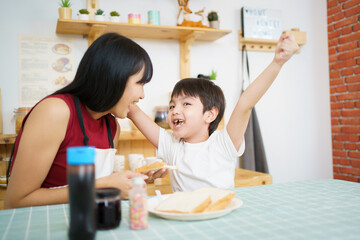 Happy little young boy and his mother making an easy breakfast together in a kitchen with a breads and chocolate jam. Mother and son playing together while making a breakfast.