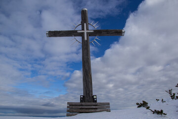  hölzernes Gipfelkreuz im winter vor weiß blauem Himmel