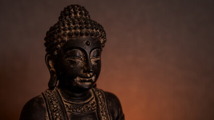 Statue of Buddha close-up in a dark environment with golden background illuminated by candlelight. Empty space for text on the right