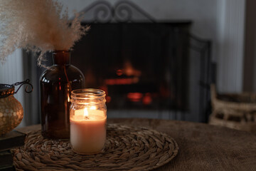 candle mock-up on wooden table and pampas grass with fireplace in background