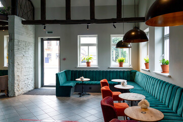 A modern cozy restaurant with colorful upholstered chairs and comfortable sofas. Unusual cafe design with rough concrete walls and wooden decorative beams on the ceiling.