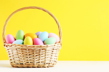 Different colorful easter eggs in basket on yellow background