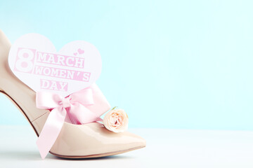 Fototapeta na wymiar Flower of rose, gift and card in shape of with text 8 March Women's Day, and beige high-heeled shoe on blue background