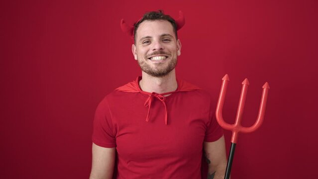 Young caucasian man smiling confident wearing devil costume over isolated red background