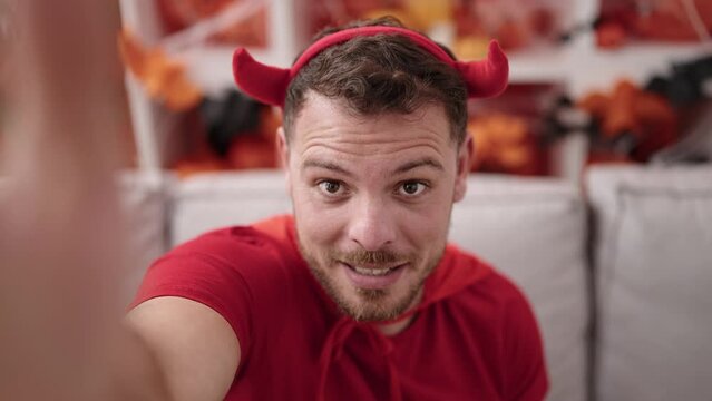 Young caucasian man wearing devil costume taking selfie picture at home