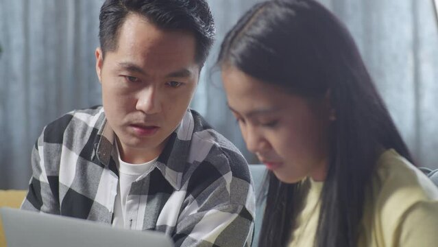 Close Up Of Asian Father Shouting At His Daughter Using A Laptop With Nonsense Things On A Sofa In The Living Room At Home
