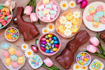 Fototapeta na wymiar Easter candies. Top view table scene over a wood background. Chocolate bunnies, candy eggs and a variety of sweets.