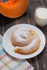 Ready-made vertuta with pumpkin lies on a plate, next to it there is a piece of pumpkin and a glass of milk