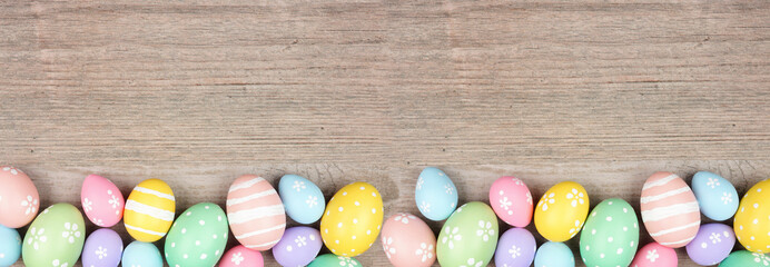 Colorful pastel Easter egg bottom border. Top down view on a light wood banner background. Copy...
