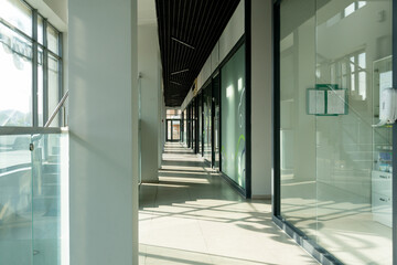 A corridor in an urban-type office building. Modern interior of the lobby of an office building with glass doors, walls and large spacious windows. A lighted long corridor in a modern business center