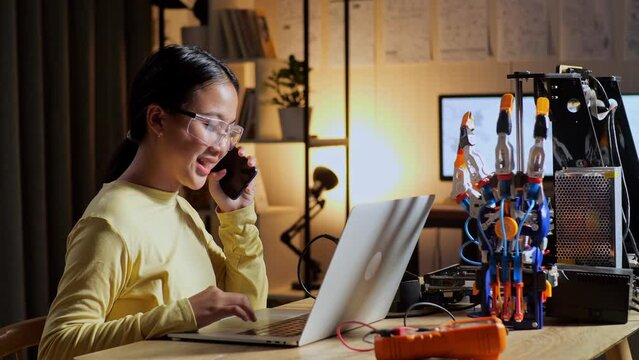 Teen Asian Girl Talking On Smartphone While Working About A Cyborg Hand On A Laptop At Home
