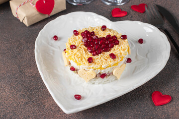 Festive puff salad with rice, chicken, eggs and cheese, garnished with pomegranate in heart-shaped plate for Valentine's Day