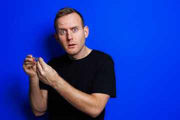 A young man in a black T-shirt on a blue background stands with a thermometer in his hands. An...