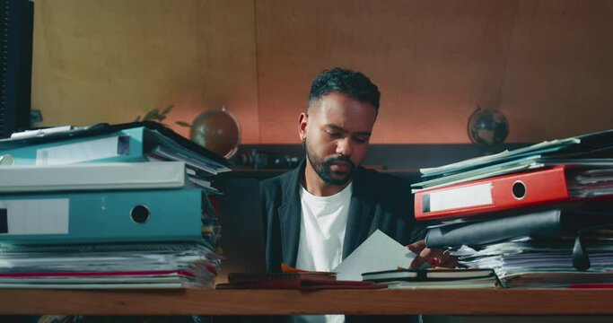 Busy focused male boss, finance manager works at office table full of paperwork documents thinking hard of solution.