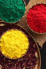 Top view of Colorful organic dry powder abeer gulal in traditional brass bowl with dry rose petals in brass plate for the celebration of Holi festival of colors in India