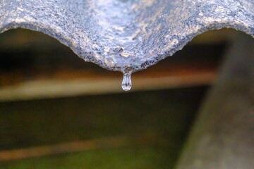 Naklejka na ściany i meble A drop of water from the edge of the roof. The beauty of winter nature. Slate is an environmentally friendly material