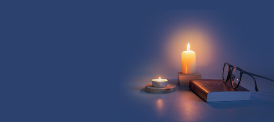Glasses and Bible with candle flame in the dark. Banner format with copy space