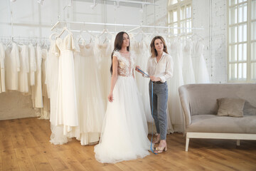 Fototapeta premium Woman trying on wedding dress with female friends having fun and taking photographs.