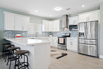 White Coastal kitchen with stainless steel appliances and sea glass backsplash tile. 
