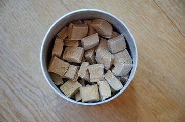 On a parquet floor, a round box filled with brown colored pills, top view.