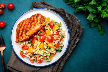 Roasted chicken breast with tabbouleh salad with bulgur, tomatoes and parsley with oil lemon dressing, green table background, top view