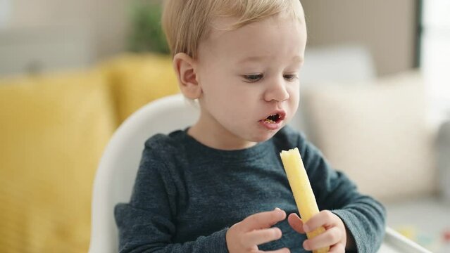 Adorable blond toddler sitting on highchair eating snack at home