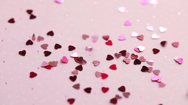 Pink and red heart shaped confetti falling on a pink surface