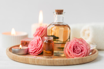 Aromatherapy. Concept of pure organic essential rose oil. Elixir with plant based floral or herbal ingredients. Pink flowers extract. Spa atmosphere with candle, towel. White background - obrazy, fototapety, plakaty