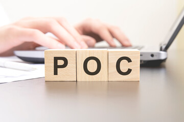poc - acronym from wooden blocks with letters. background hands on a laptop with blur. business...