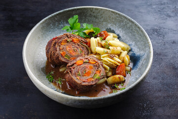 Traditionelle slow cooked deutsche Wagyu Rinderrouladen mit Gnocchetti-Sardi Nudeln in würziger Bratensoße als close-up auf einem Nordic Design Teller 