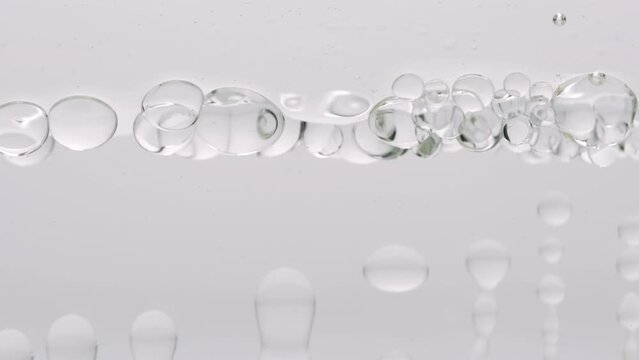 Macro shot of grey clear bubbles form and float to another ones on grey transparent liquid surface on grey background | Abstract skin moisturizing products formulation concept