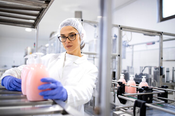 Female factory worker in white sterile uniform and hairnet working for pharmaceutical company and producing liquid soap cleaning chemicals.