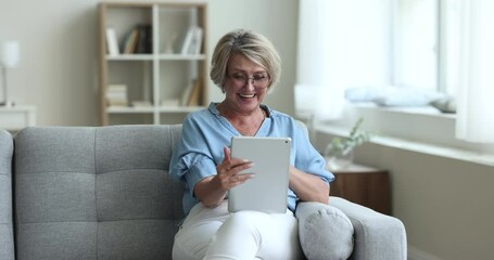 Aged woman makes video call, sits on sofa with digital tablet, greeting grown up children enjoy pleasant talk to family living abroad use videoconference app. Virtual meeting event with beloved people