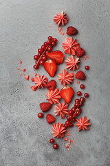 Small pink meringues and various red berries on gray concrete background. Top view, flat lay