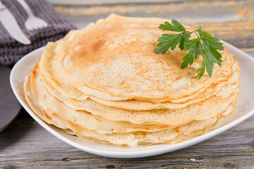 Pile of crepes decorated with a parsley leaf on a wooden table	

