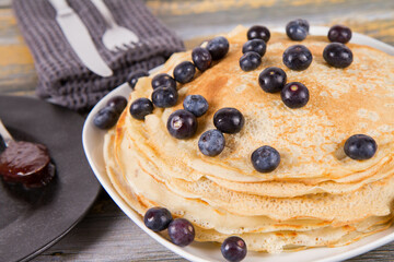Pile of crepes with blueberry fruit with some jam on the side on a wooden background
