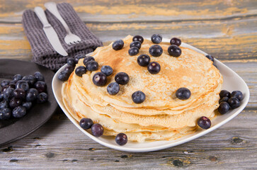 Pile of crepes with blueberry fruit on a wooden background