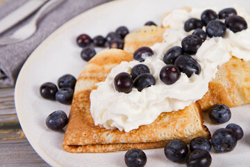 Crepes with blueberry fruit and whipped cream on a wooden background