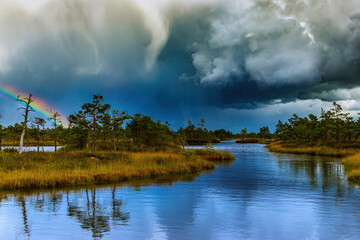 Landscape of a national park before a thunderstorm.The beauty of nature.Heavy dark beautiful blue clouds,bright rainbow,blue river and green grass and trees.Nature before the storm.Warm summer day.