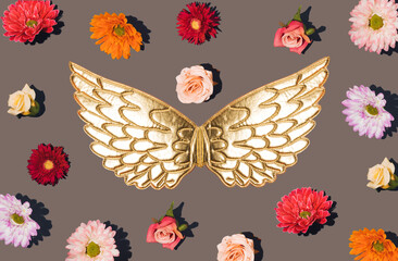 Golden angel wings and many flowers on a gray background. Minimal spring concept
