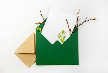 Spring flat lay. Postal envelopes with spring decor for design. Envelope with blank sheet and twigs. Mockup of invitation on white background. Blank white card and envelope from craft paper. Top view.