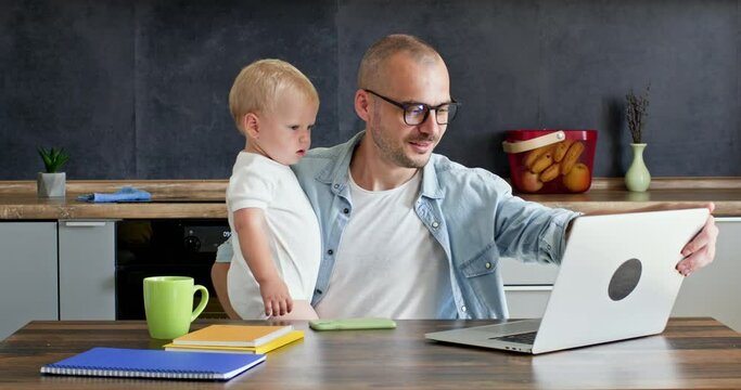 A man on maternity leave works at home with a child in his arms.