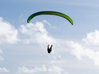 A paraglider can be seen hanging upside down in his harness with a green wing above shot against a...