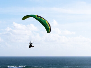A paraglider can be seen gliding in his harness with a green wing above shot against a blue sky...
