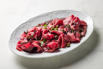 Sliced roast beef on white plate on white marble table macro close up