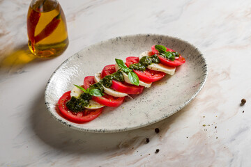 Caprese salad with mozzarella cheese, tomato, basil and sauce pesto on plate on marble table
