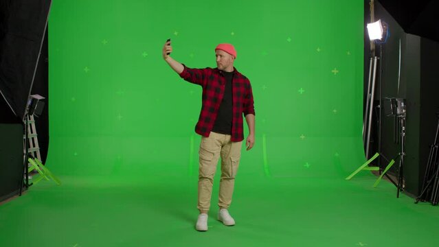 Full body video shot of man dressed casual clothes taking selfie on smartphone on green screen background, chroma key