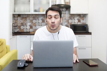 Young happy man in earphones looking at laptop and talking on video call. Online dating concept