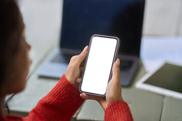 Over shoulder view of woman student or worker holding mobile phone with white blank mock up cell...